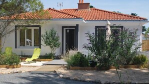 A single-story house with a red-tiled roof, a front door, and a small porch area with a chair and plants.