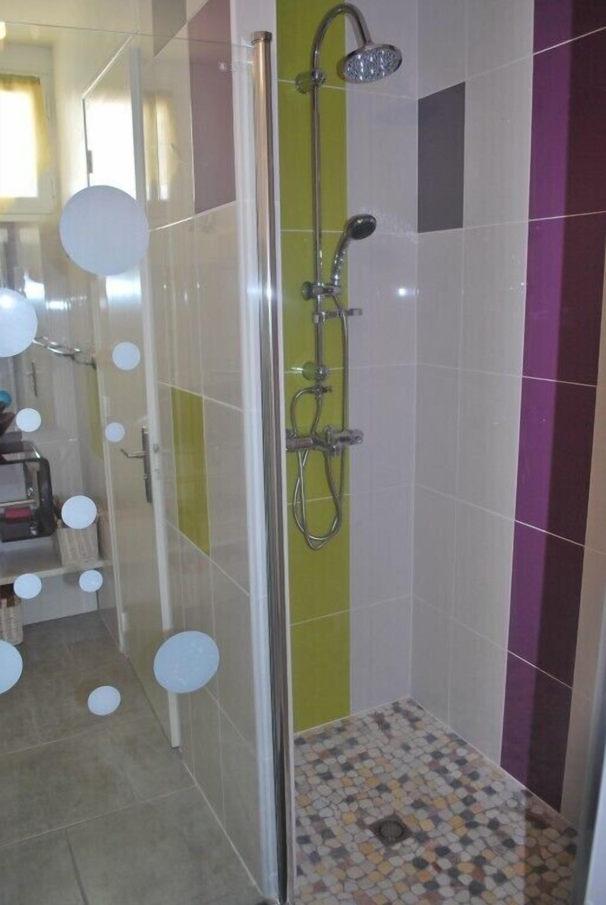 A shower area with a glass door, a handheld showerhead, and a tiled floor.