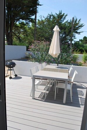 Een terras met een tafel, stoelen, een parasol en een barbecue.