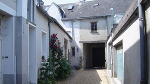 A narrow alleyway between buildings with gravel ground, potted plants, and a door at the end.
