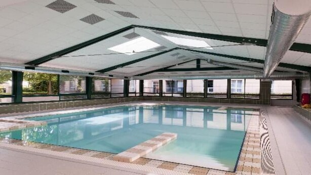 Une piscine intérieure avec un sol carrelé, un plafond transparent doté de lucarnes et un mur en briques.