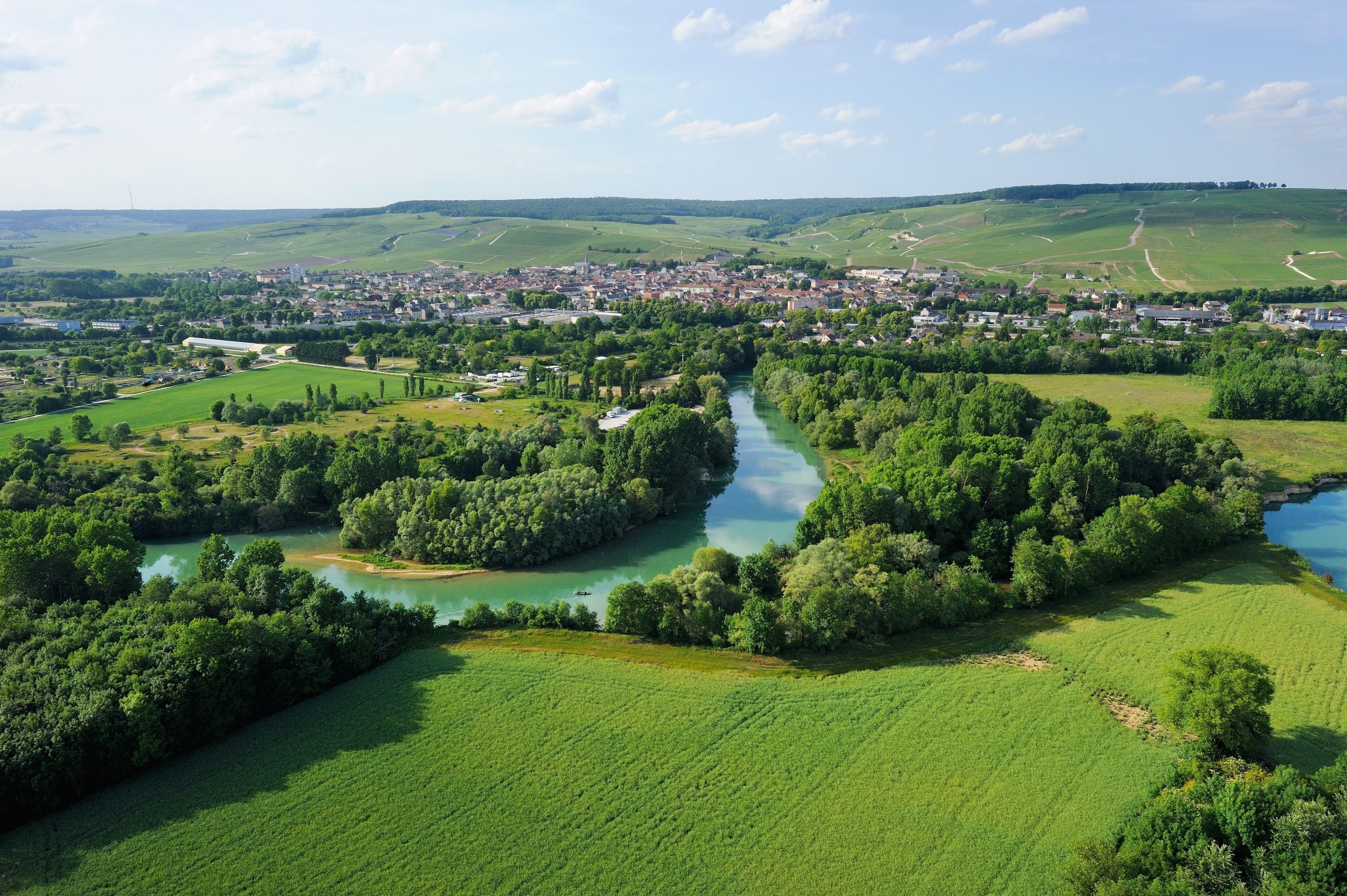 Une rivière serpente à travers une ville entourée de champs verdoyants et de collines.