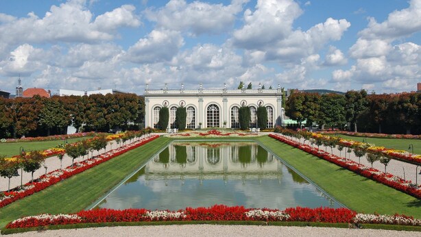 Een statig gebouw met een symmetrische tuin en een fontein in het midden.