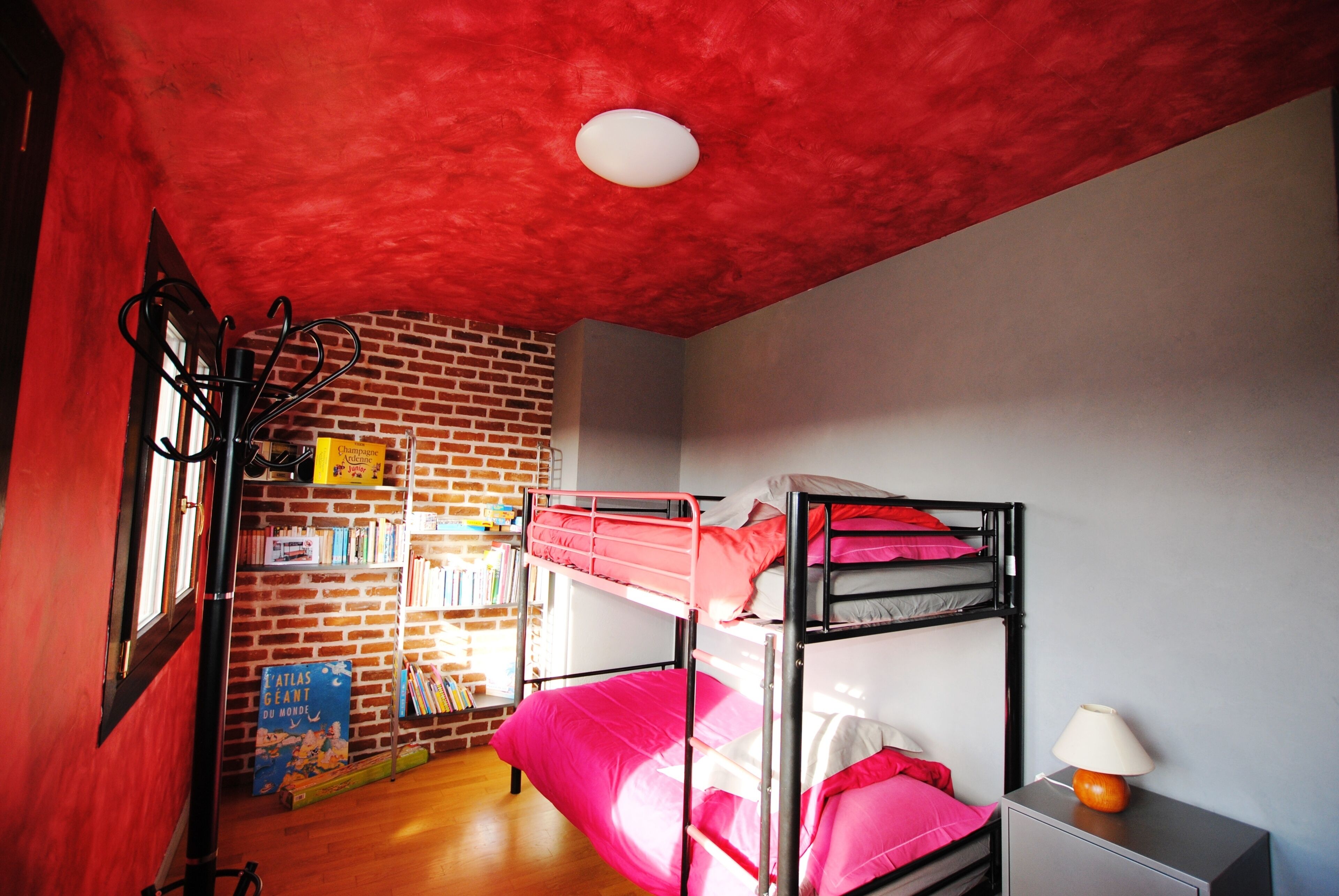 Une chambre avec un lit superposé, une bibliothèque, un bureau avec une lampe et un plafond rouge.