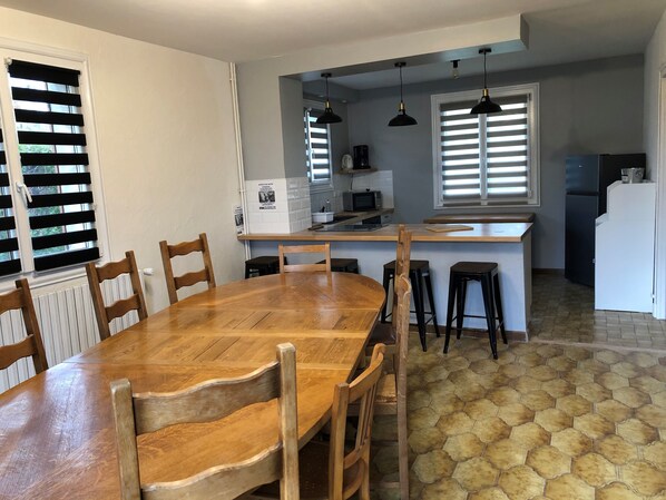 A dining area with a wooden table and chairs, a kitchen with a microwave and refrigerator, and a tiled floor.