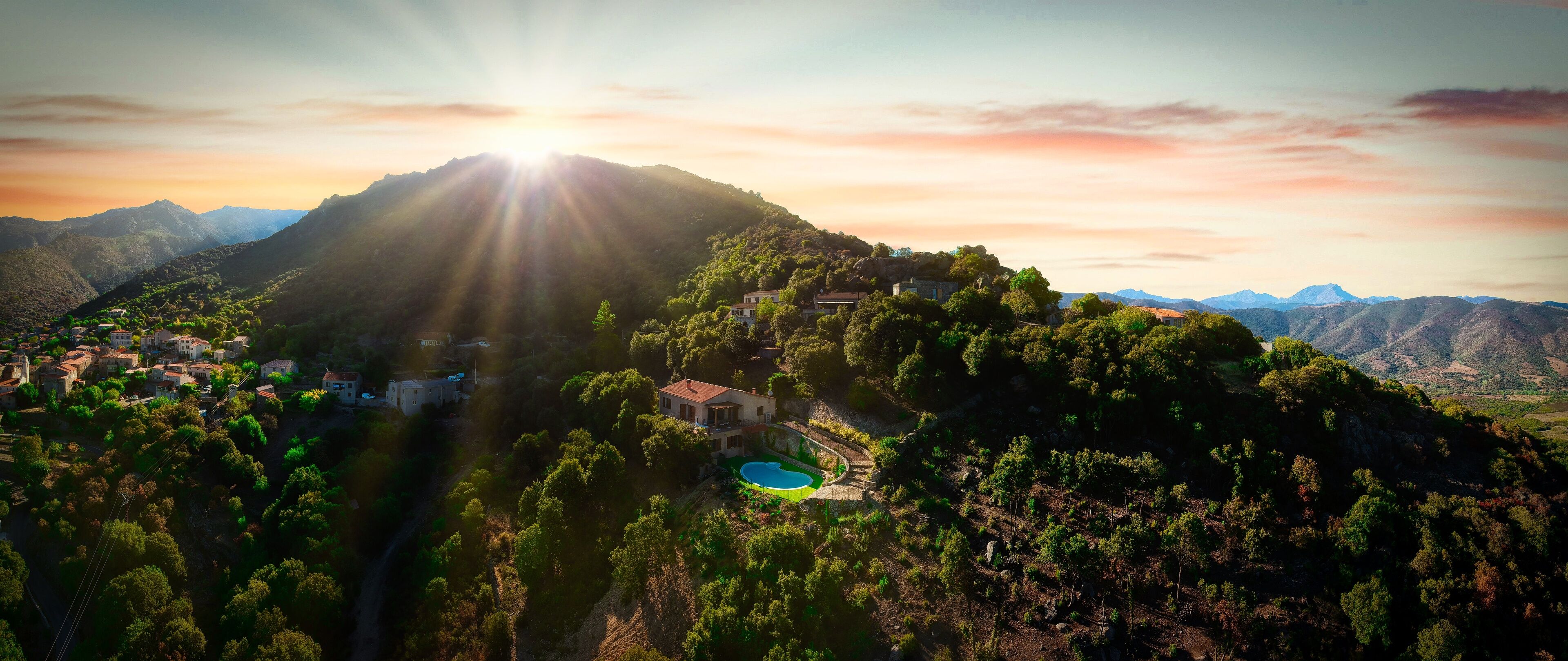 A mountainous landscape with a village, a swimming pool, and houses with red roofs.
