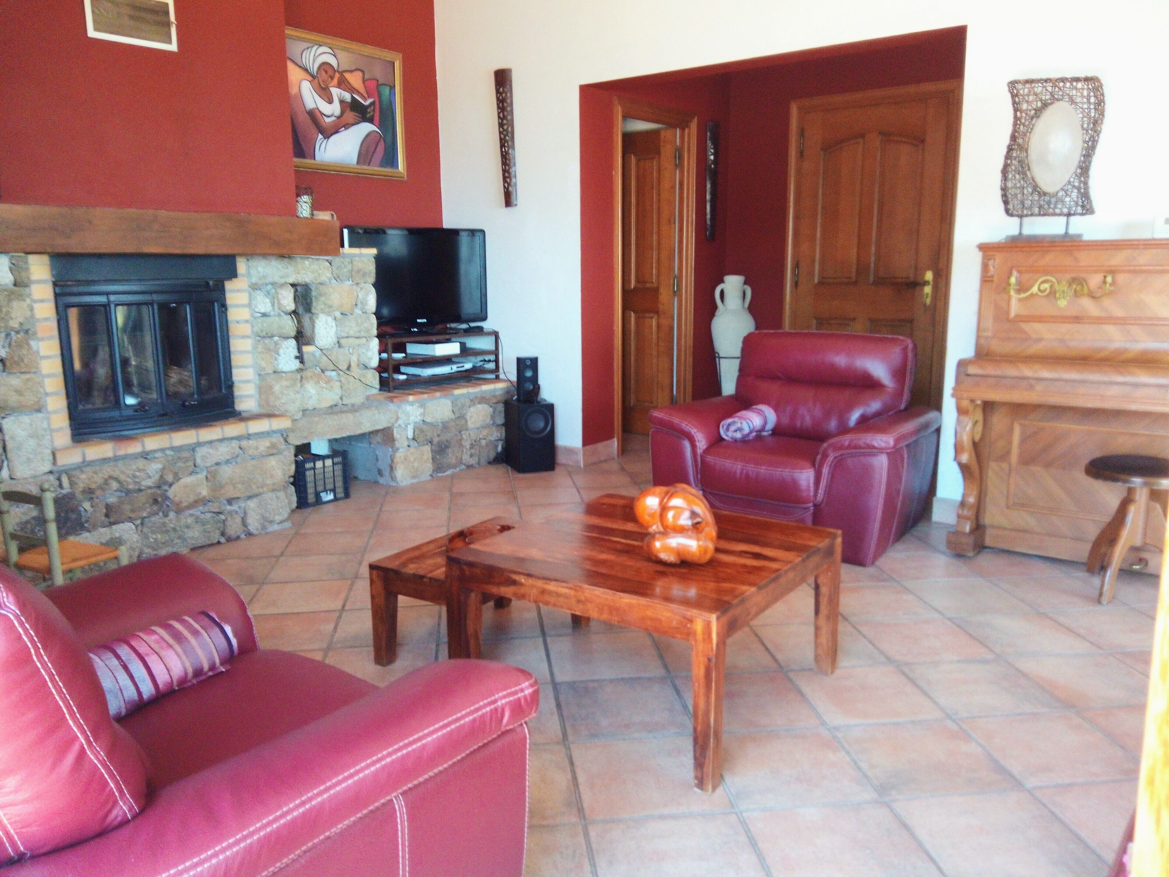 Un salon avec une cheminée en pierre, un canapé en cuir rouge, une table basse en bois et un fauteuil en cuir rouge.