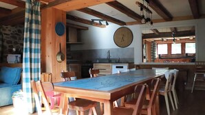 Eine rustikale Küche mit Holzbalken, einer großen runden Uhr und einem Essbereich mit langem Tisch und Stühlen.
