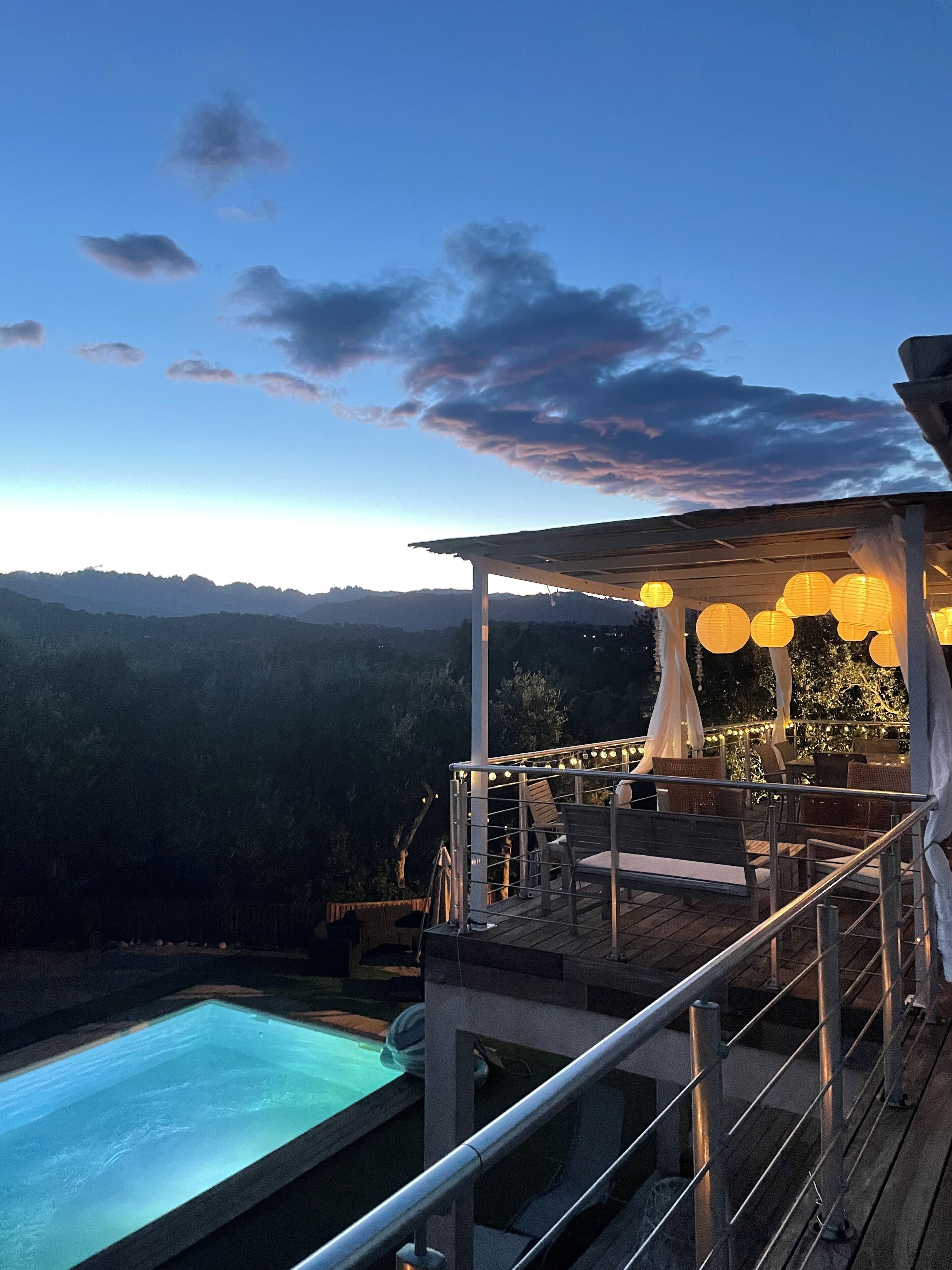 A poolside area with a view of the mountains, outdoor seating, and string lights.