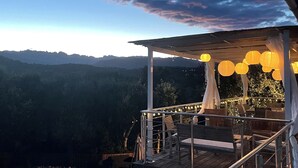 Zona de piscina con vistas a las montañas, mobiliario exterior y luces colgantes.