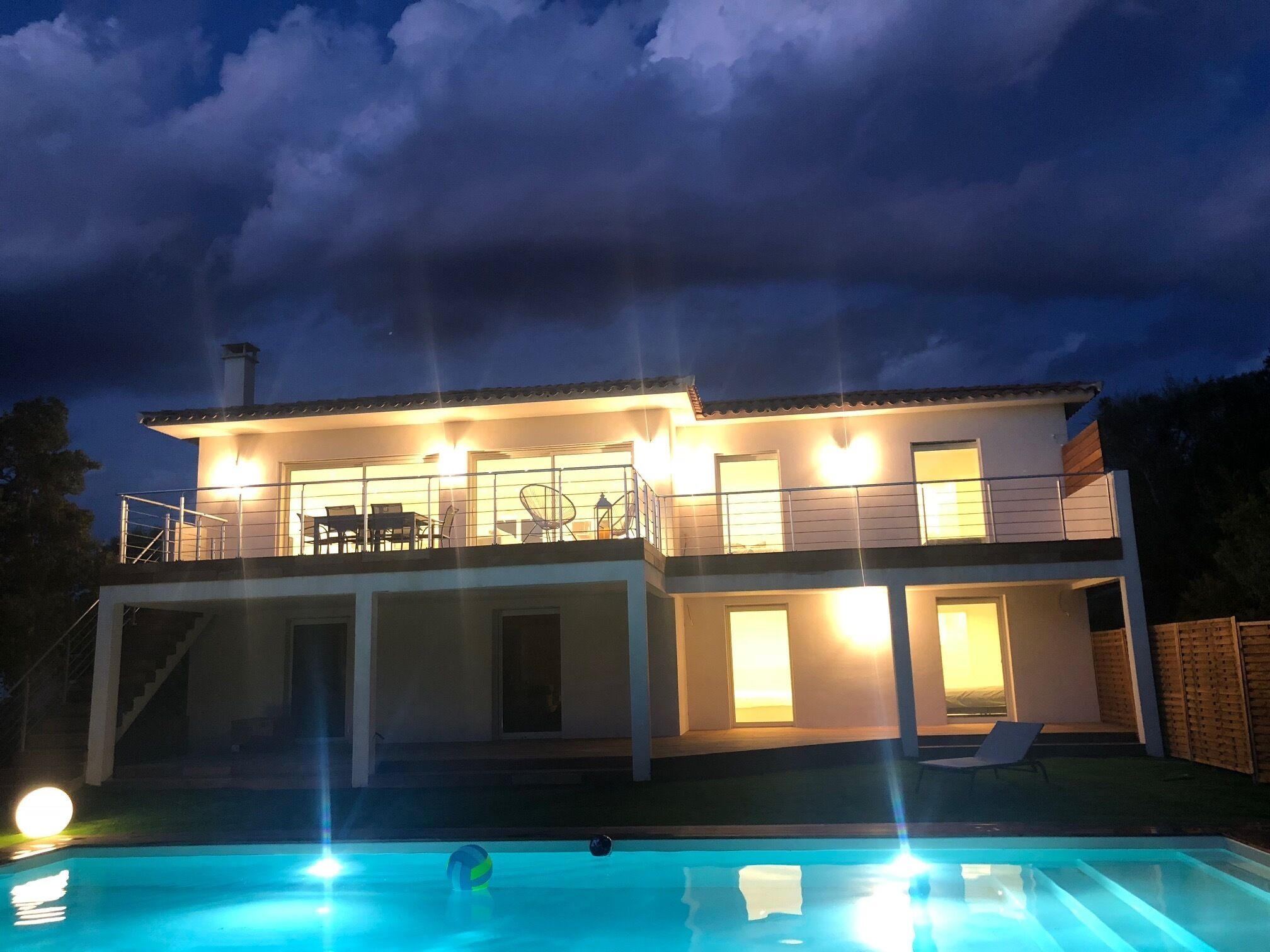 Una casa de dos pisos con balcón, piscina e iluminación exterior.