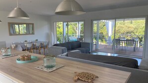 Una sala de estar moderna con una mesa de comedor de madera, un sofá gris y un amplio ventanal con vistas al exterior.