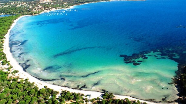 Vista aérea de una zona costera con playa, aguas cristalinas y vegetación circundante.