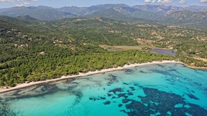 Vista aérea de una zona costera con playa, aguas turquesas cristalinas y colinas verdes circundantes.