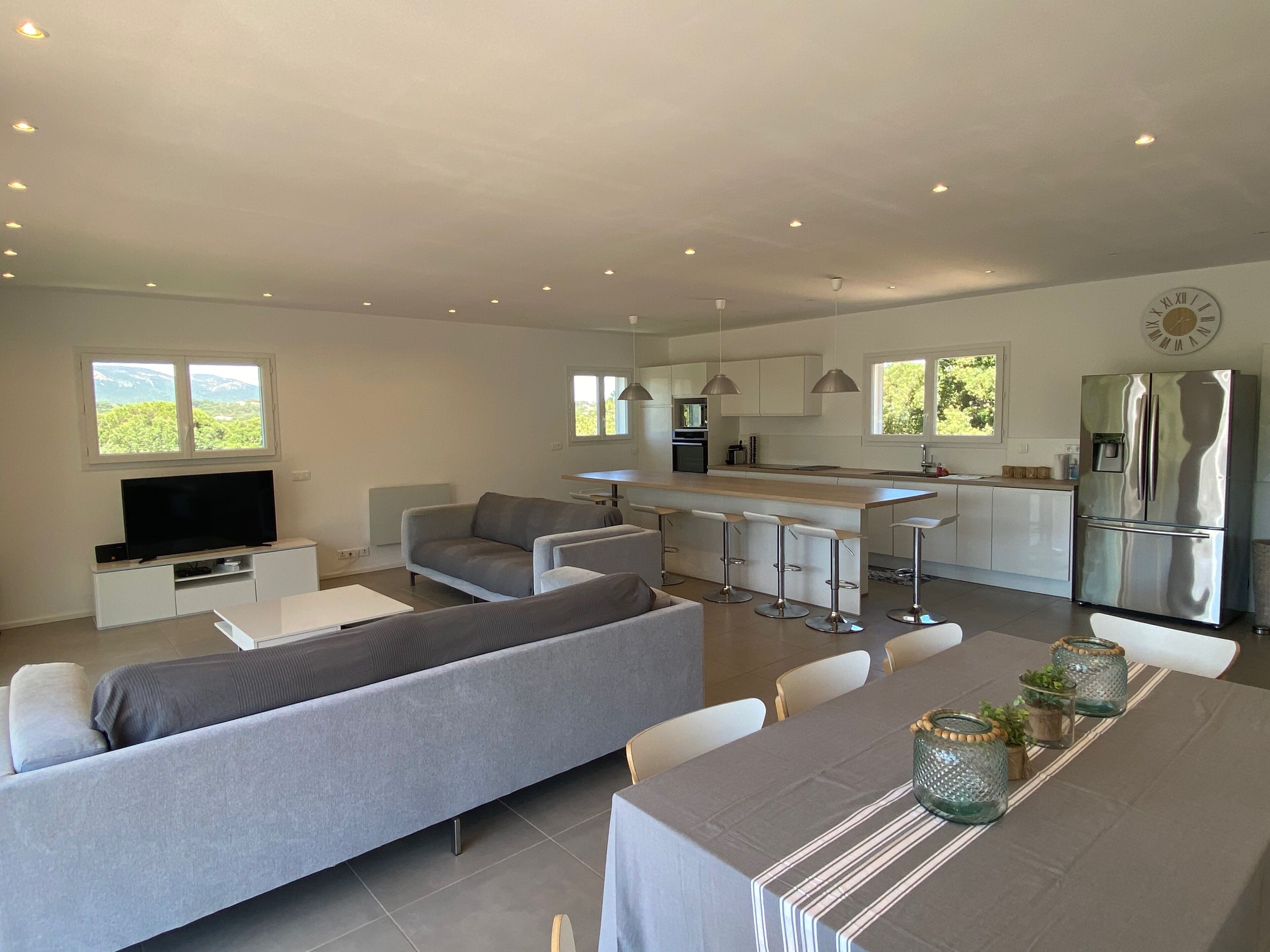 Un espace de vie moderne comprenant un canapé, un téléviseur, une table à manger, une cuisine et un coin bar.