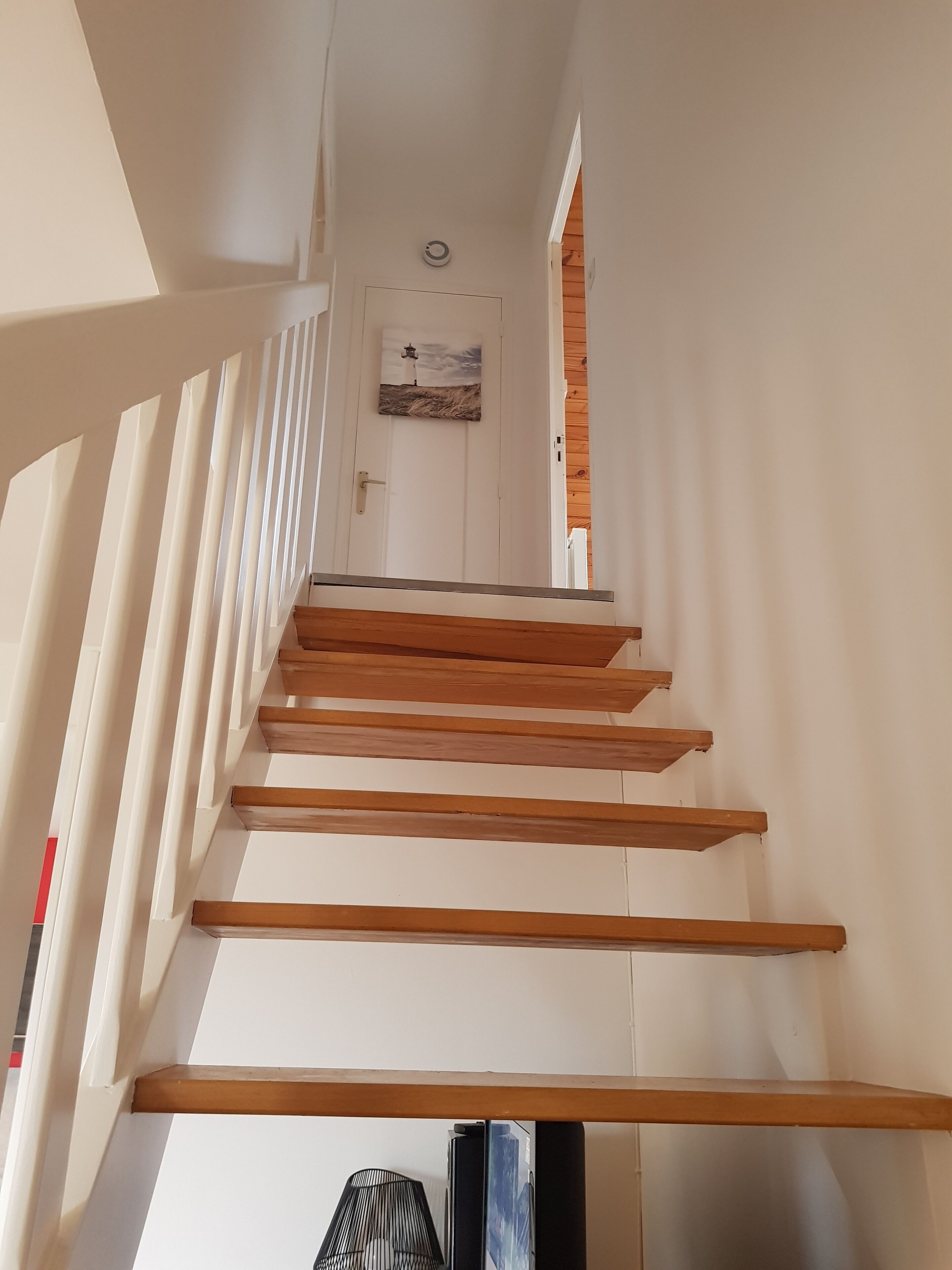 A staircase with wooden steps and white walls, leading to a door with a painting of a lighthouse.
