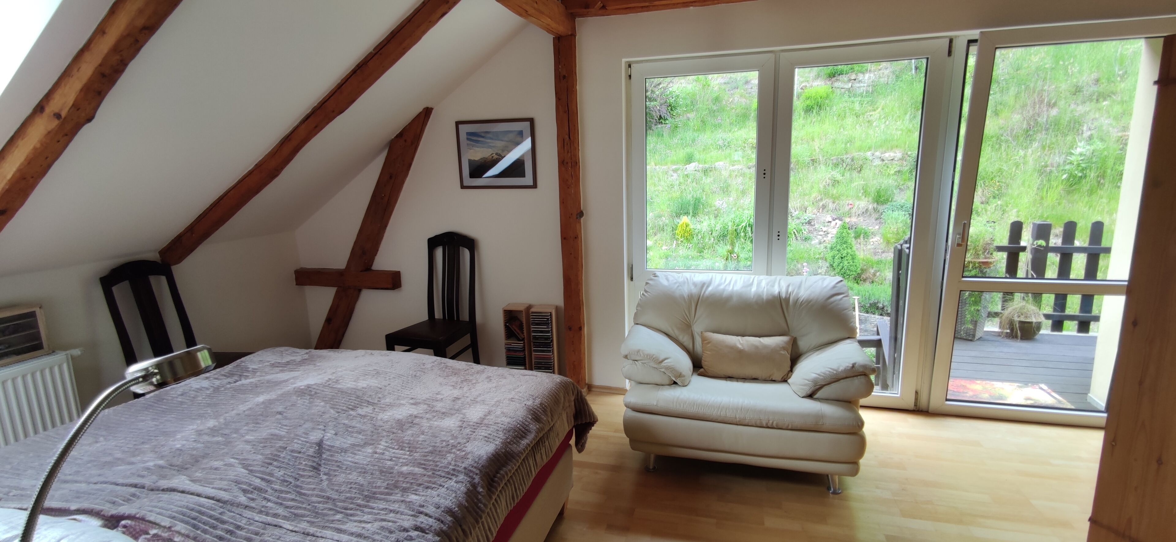 Een slaapkamer met een bed, een stoel, een foto aan de muur en een schuifdeur naar buiten.