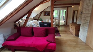 A cozy room with a red sofa, wooden beams, a white radiator, and a view through a window. - Stylishly furnished apartment in Rathmannsdorf in the Zauketal, allergy sufferers (Rathmannsdorf)