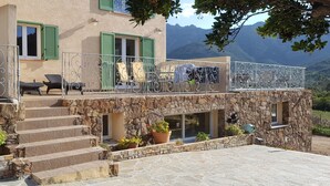 Ein Steinhaus mit Balkon, Stufen, die zu einer Tür führen, und Außenbestuhlung.