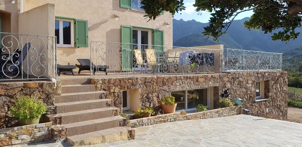 A stone building with a balcony, steps leading to a door, and outdoor seating.