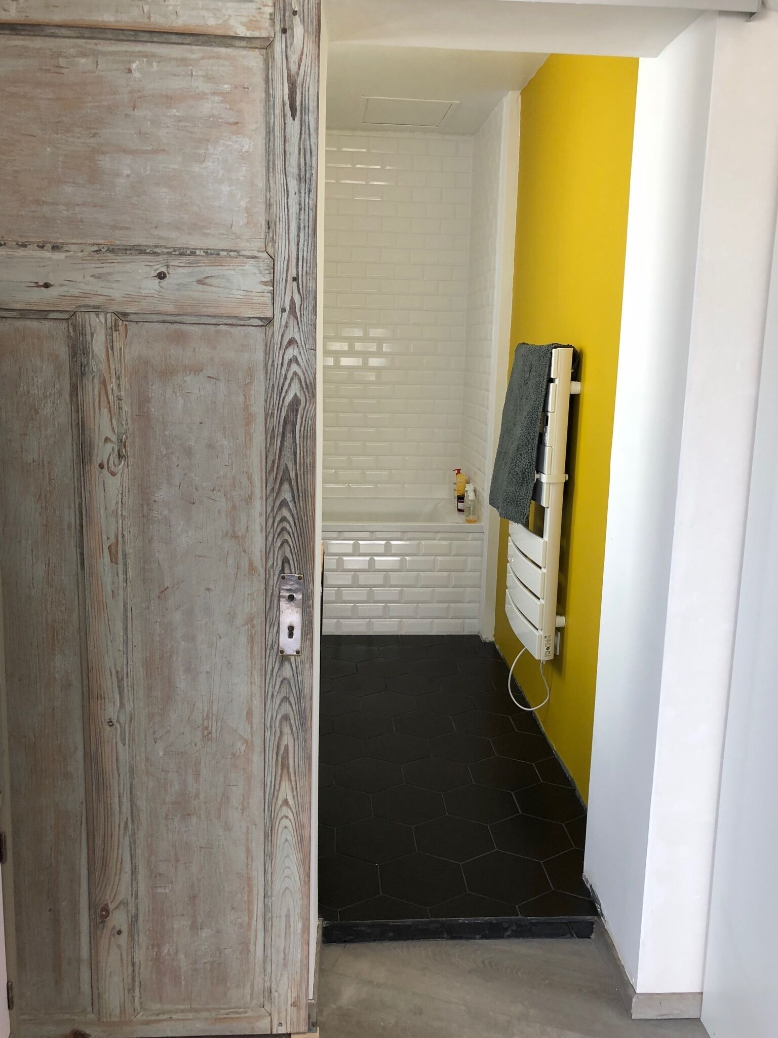 A bathroom with a shower, a towel rack, and a wooden door.