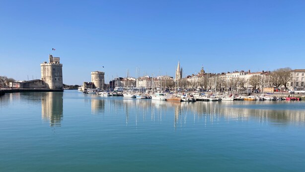 A marina with boats docked, a historic tower, and a cityscape with buildings and a church. - ☼ La Siesta ☼ Character house with garden and terraces ☼ (La Rochelle)
