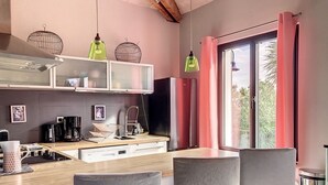 A modern kitchen with a wooden countertop, a coffee machine, and a sink. There are two chairs and a table in front of a large window with red curtains. - ☼ La Siesta ☼ Character house with garden and terraces ☼ (La Rochelle)