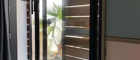 Un interno moderno con una porta scorrevole in vetro che dà su uno spazio esterno, un pavimento chiaro e una vista parziale di una stanza con un mobile scuro.