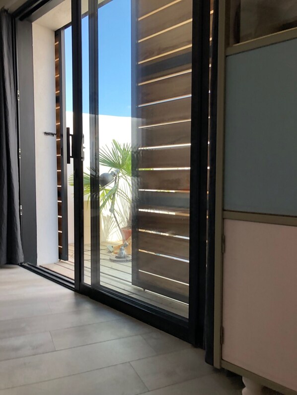 A modern interior with a sliding glass door leading to an outdoor area, a light-colored floor, and a partial view of a room with a dark-colored cabinet.