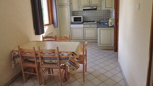 A compact kitchen with a dining area, featuring a table with chairs, a microwave, a stove, and cabinets. - Rental cottage in renovated farm (Arrentès-De-Corcieux)