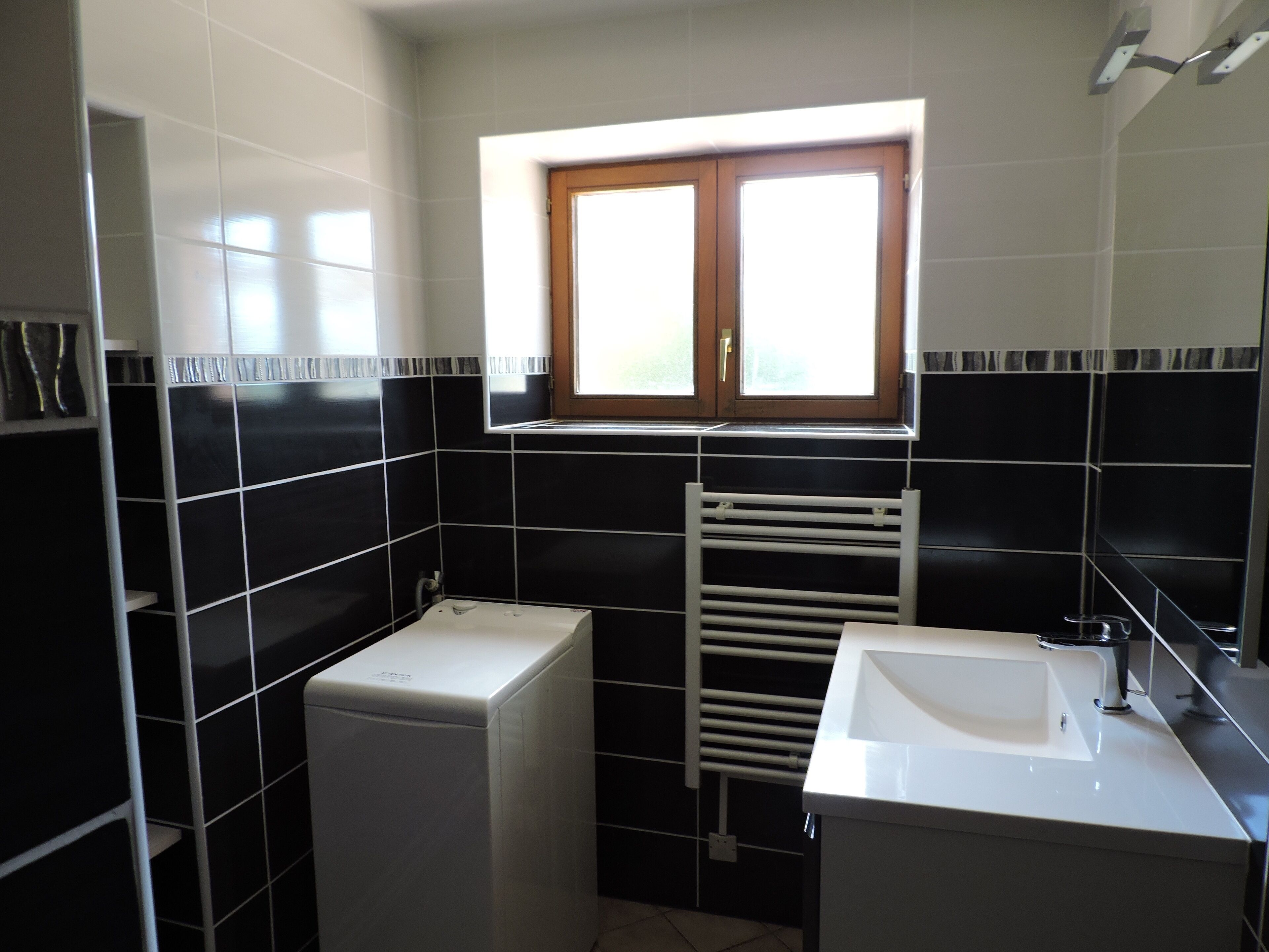 A bathroom with black and white tiles, a window, a towel rack, and a sink.