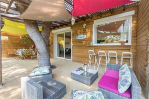 An outdoor seating area with wicker furniture, a red umbrella, and a wooden wall. - Félyvonne, family villa with sea and vineyard view (Hyères)