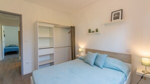 A bedroom with a bed, bedside lamps, a wardrobe, and a small shelf with decorative items. - Félyvonne, family villa with sea and vineyard view (Hyères)