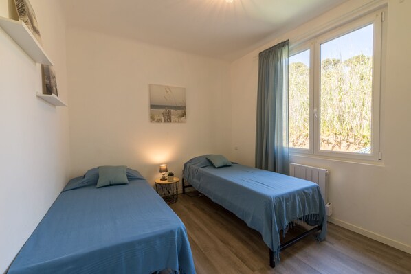 A room with two single beds, a small bedside table with a lamp, a painting on the wall, and a window with curtains. - Félyvonne, family villa with sea and vineyard view (Hyères)
