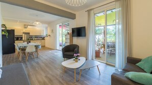 A modern living room with a dining area, a kitchen in the background, and a large sliding glass door leading to an outdoor patio. - Félyvonne, family villa with sea and vineyard view (Hyères)