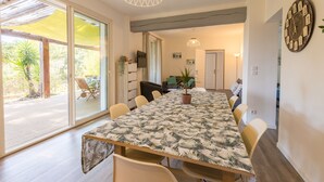 Un espace repas comprenant une grande table, des chaises et une vue sur une terrasse extérieure, accessible par des portes vitrées.