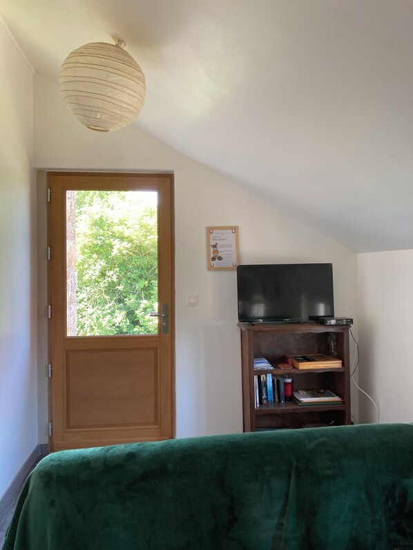 A room with a wooden door, a television on a wooden stand, and a green blanket on the bed.