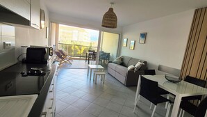 A modern kitchen with a dining area, a balcony with a view of buildings, and a living area with a sofa and a table. - CALVI T2 terrace for 4. Close to beaches, the city centre and all facilities (Calvi)