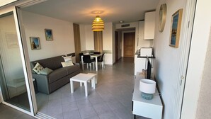 A modern living room with a sofa, coffee table, and a dining area with chairs. - CALVI T2 terrace for 4. Close to beaches, the city centre and all facilities (Calvi)