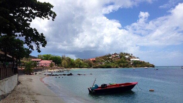 A beach with a boat, clear water, and a building in the background. - RESIDENCE VERY CALM  (Anse mitan)