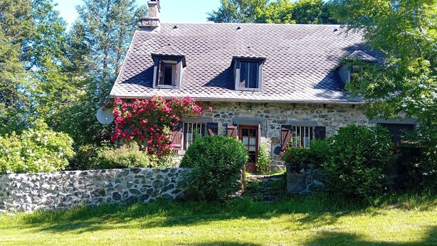 Ein Haus aus Stein mit einem geneigten Dach, zwei Fenstern und einer Steinmauer davor.