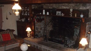 A cozy living room with a stone fireplace, a sofa, a coffee table with a vase, and a bookshelf with various items. - Old farmhouse restored warm decoration comfortable on a 3ha plot (Saint-Donat)