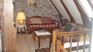 A cozy attic room with a stone wall, a wooden sofa, a small table with a lamp, and a wooden chair. - Old farmhouse restored warm decoration comfortable on a 3ha plot (Saint-Donat)