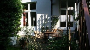 A garden with a wooden bench and a table, surrounded by potted plants and a white building with windows. - beautiful apartment in good location with well connection to all landmarks  (Hamburg)