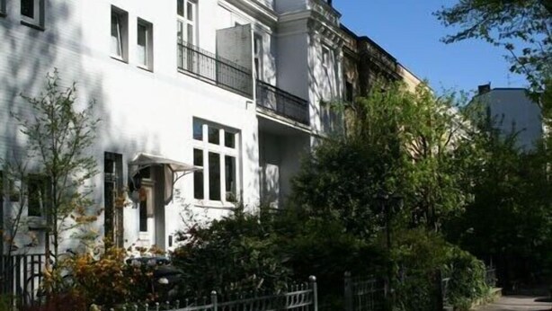 A two-story building with a white facade, a balcony on the second floor, and a metal fence in front. - beautiful apartment in good location with well connection to all landmarks  (Hamburg)