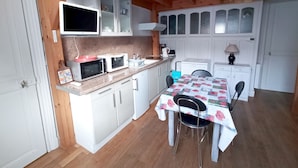 Een kleine keuken met witte kastjes, een magnetron, een waterkoker en een tafel met stoelen.