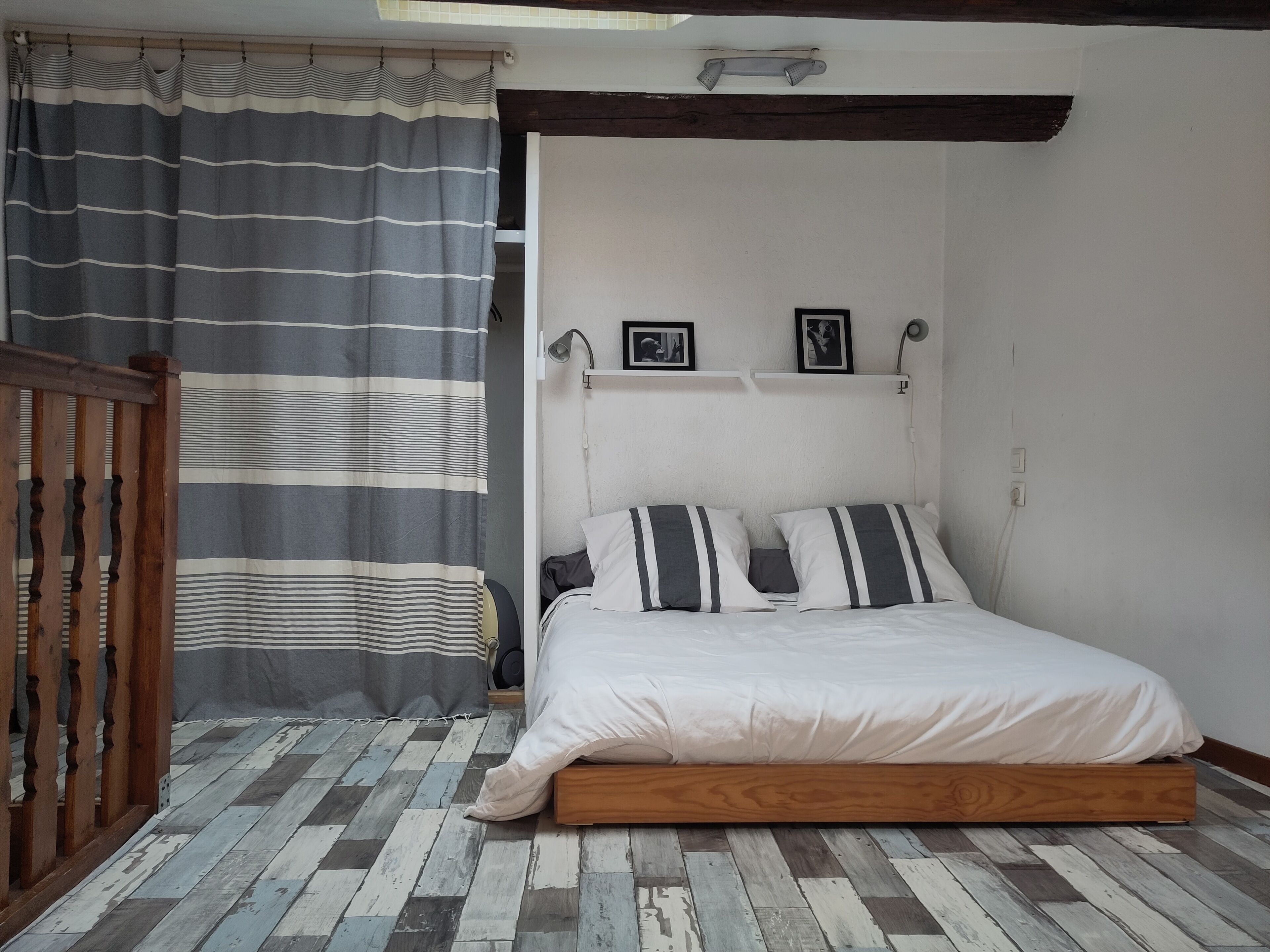 Un dormitorio con cama, piso de madera y cortina a rayas.