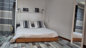Ein Schlafzimmer mit einem hölzernen Bettgestell, gestreifte Vorhänge und einem Spiegel, der das Bett reflektiert.