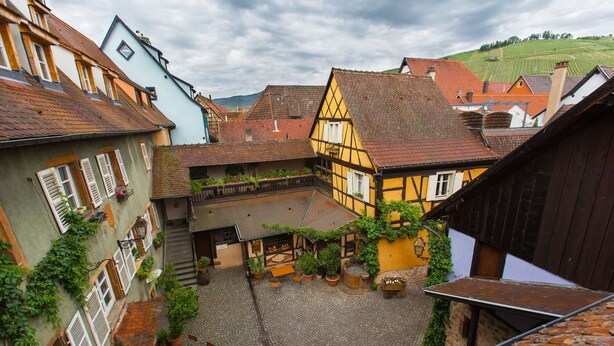 Una estrecha calle adoquinada en un pueblo tradicional europeo, con edificios de entramado de madera y un pequeño patio.