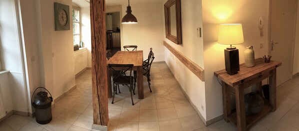 A hallway with a wooden dining table and chairs, a lamp on a side table, and a large wooden beam structure.